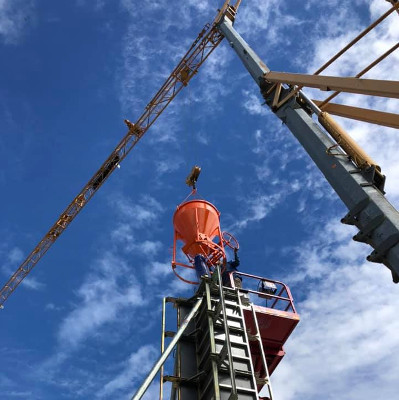 Eine Baustelle mit einem Kran, der einen orangefarbenen Aufzug transportiert, vor einem blauen Himmel.